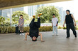 © DragonImages - Group of young people practicing breakdance under modern city overpass with trees and buildings in background, breakdancer in center performing upside down move, wearing yellow shoes