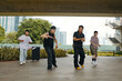 © DragonImages - Group of dancers performing under an overpass in urban area featuring greenery and city skyline in background showing diverse moves and sharing energy