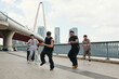 © DragonImages - Group of young men dancing energetically beside modern bridge under clear sky capturing urban lifestyle and movement dynamics with background of city skyline and high-rise buildings