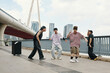 © DragonImages - Group of dancers sharing energetic moves on modern urban bridge surrounded by skyscrapers on partly cloudy day, expressing passion for street dance and joy of movement