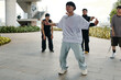 © DragonImages - Group of friends performing dance routine in urban setting with industrial backdrop and greenery. Dancers dressed casually, showing synchronized movements and energy