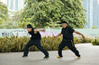 © DragonImages - Two men practicing martial arts in urban park, posing dynamically amidst urban greenery and graffiti background, showcasing their athletic skills