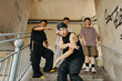 © DragonImages - Group of young friends dancing energetically under urban bridge, showcasing street fashion. Visible graffiti art adds to the urban vibe