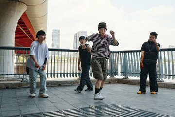 Group of young men performing energetic dance routine under urban bridge background Sturdy bridge structure visible while dancers showcase vibrant moves in laid-back attire