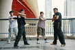 © DragonImages - Group of friends standing together underneath urban bridge with city buildings in background, showing different poses and expressions
