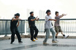 © DragonImages - Group of young men engaging in synchronized dance practice outdoors, with urban cityscape in background, showing energetic movement and coordination