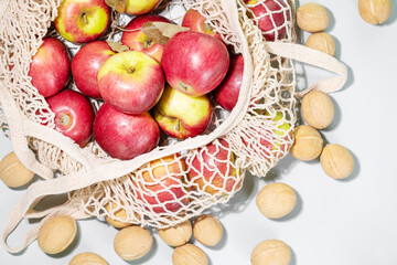 Reusable mesh bag filled with fresh red apples and surrounded by whole walnuts, emphasizing sustainable and mindful eating. Perfect for promoting healthy food choices and seasonal fruits