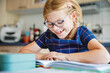 © Irina Schmidt - Little happy girl with eyeglasses reading book at home. Elementary school child reads, making homework. Education concept.