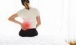 © Ton Photographer4289 - Woman holding her lower back while sitting in bed has chronic back pain. Health Care concept