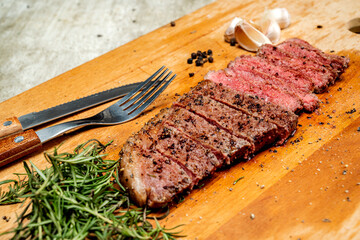 A piece of picanha meat is cut and sitting on a wooden cutting board with a fork and knife