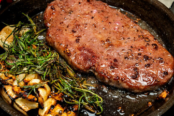 A piece of picanha meat is cooked in a pan with garlic and herbs