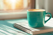 © zamuruev - The warm sunlight streams through a window, illuminating a teal coffee cup resting on a notebook, creating a calm and inviting morning atmosphere perfect for reflection