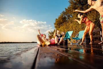 Wall Mural - Group of friends having fun drinking beer, enjoying a summer day swimming and jumping at the lake..