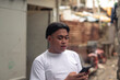 © Mdv Edwards - A young asian man chatting or browsing social media on his phone. Slum area background.