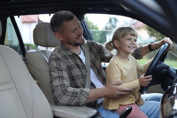 Wall Mural - Happy man with his daughter holding steering wheel inside car