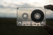 © Maxim Chuev - man holding transparent audio cassette between two male fingers on blue sky and field background. magnetic tape. old technology.