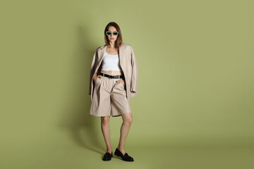 Wall Mural - Beautiful woman in stylish beige suit and sunglasses on olive background, space for text