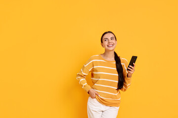 Wall Mural - Smiling woman with smartphone on yellow background. Space for text