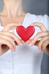 Wall Mural - Doctor holding red heart on grey background, closeup