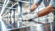 © Four888 - Polished metal surface being wiped clean with a white cloth, revealing a mirror-like finish and subtle scratches, against a blurred grey industrial background.