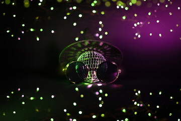 A witch hat and a disco ball and hipster sunglasses with green and purple bokeh light on a black background. Creative Halloween party wallpaper