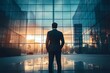 © MdRazib - A man stands in front of a modern glass business center. Back view.