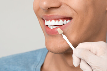 Canvas Print - Doctor checking young man's teeth color on gray background, closeup. Dental veneers