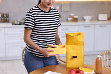 Canvas Print - Woman packing lunch box with healthy food at wooden table in kitchen, closeup. Preparing for school