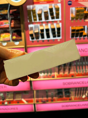 A package from cosmetic product in hand against the background of shelves with cosmetics (lipsticks, eyebrow pencils, eyeshadows, blush, mascara). Copy space, place for text, bright banner, copyright