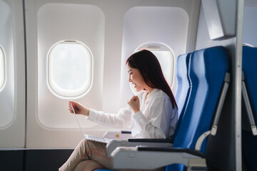 Wall Mural - In-Flight Business Triumph: Asian businesswoman celebrates success on laptop, airplane window seat, online booking, travel excitement 