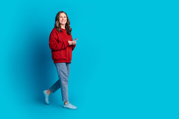 Full size photo of pretty aged lady walk use phone wear pullover isolated on blue color background