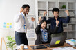 © Kritdanai - Office Triumph: Exuberant colleagues celebrate a shared success, their infectious joy radiating around a laptop in a modern workspace.