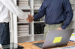 © Kritdanai - Sealing the Deal: Two business professionals solidify their agreement with a firm handshake, a laptop and office setting in the background hinting at a successful collaboration.