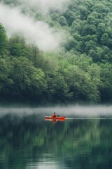 A man kayaking in still lake water with forest and fog