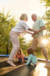 © Iuliia Versta/Stocksy - a senior couple with two grandchildren jumping on a trampoline