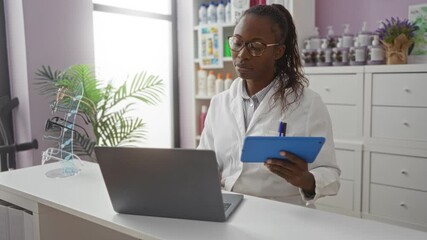 Canvas Print - Female pharmacist working on a computer and tablet in a well-lit pharmacy interior with glasses display and products on shelves