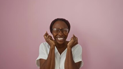 Sticker - Luck smiling, young african american woman wearing glasses, fingers crossed, eyes closed in hope, gesturing over isolated pink background, superstitious and standing happy