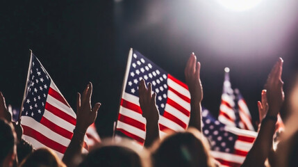 People raise their hands holding American flags during an evening event, capturing the spirit of patriotism and celebration.