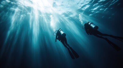 An immersive underwater shot of two scuba divers navigating through the depths as beams of light penetrate the water, illuminating the scene and creating an awe-inspiring experience.