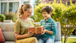 © NewFresh  - happy mother and son with gift box sitting on sofa in garden at home