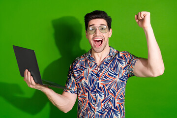 Poster - Photo of overjoyed guy with bristle stylish haircut dressed print shirt in glasses hold laptop win bet isolated on green color background