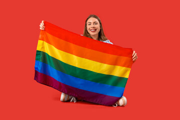 Wall Mural - Young woman with LGBT flag sitting on red background