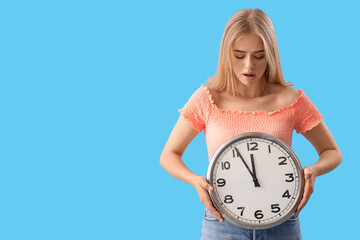 Canvas Print - Stressed young woman with clock on blue background. Deadline concept