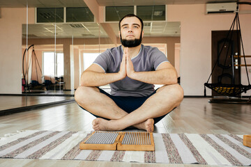 Man exercising yoga meditating sitting hands joined on the floor near sadhu board