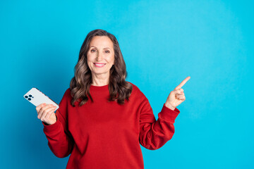 Sticker - Photo of pretty aged lady hold phone indicate finger empty space wear red pullover isolated on blue color background