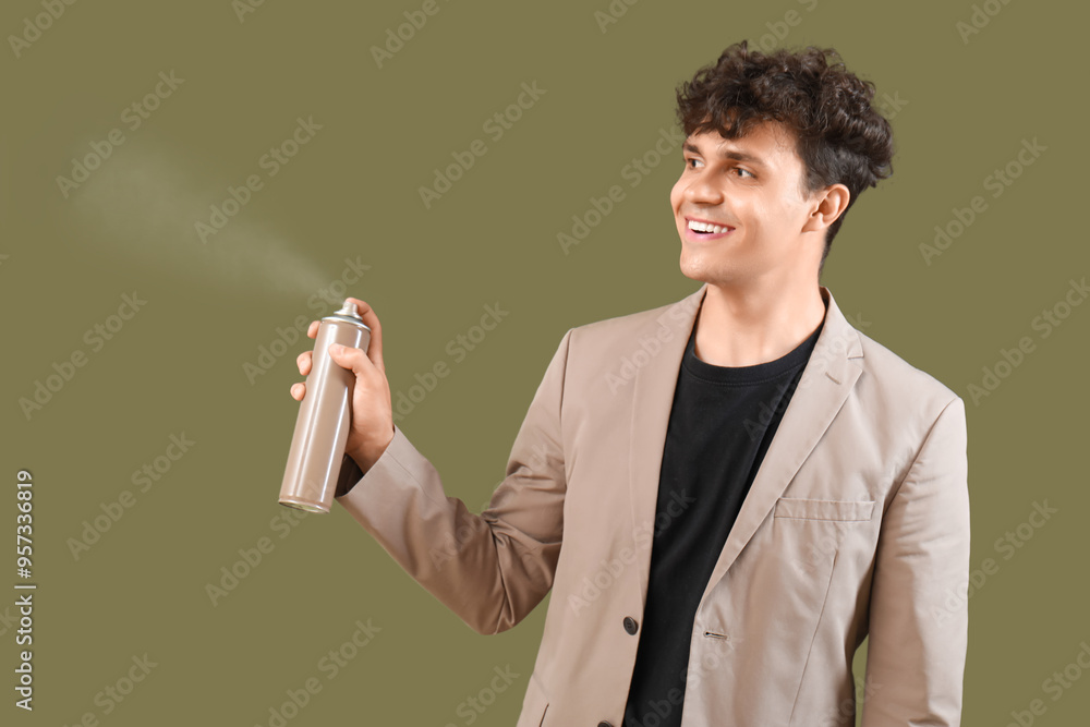 Handsome young man using bottle of hair spray on green background