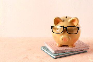 Piggy bank in eyeglasses with books on grunge pink table near wall