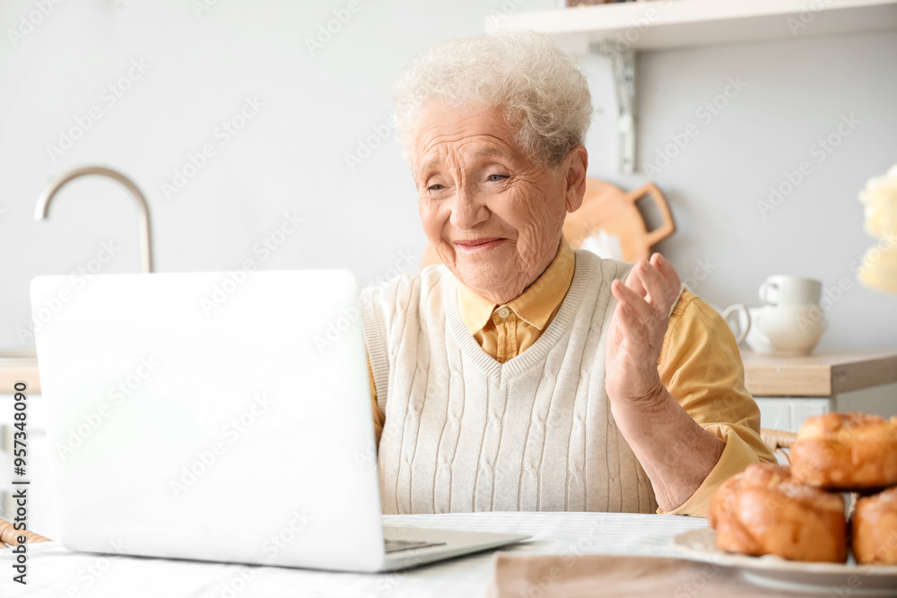 Senior woman using laptop at table in kitchen