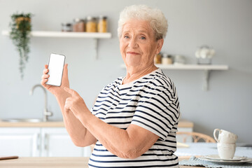 Poster - Senior woman pointing at mobile phone in kitchen