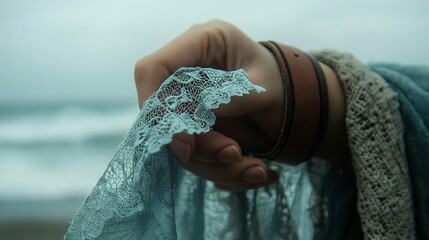 Poster -   A person holds a piece of lace against a serene water backdrop with rippling waves